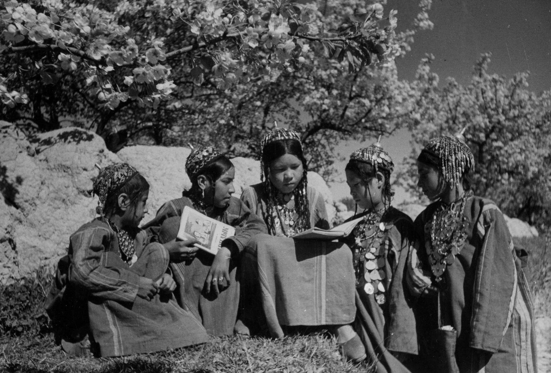 Girls in traditional clothing reading together under a tree