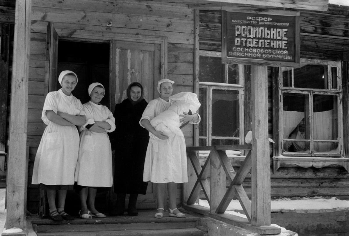 four women on porch, one holding swaddled baby