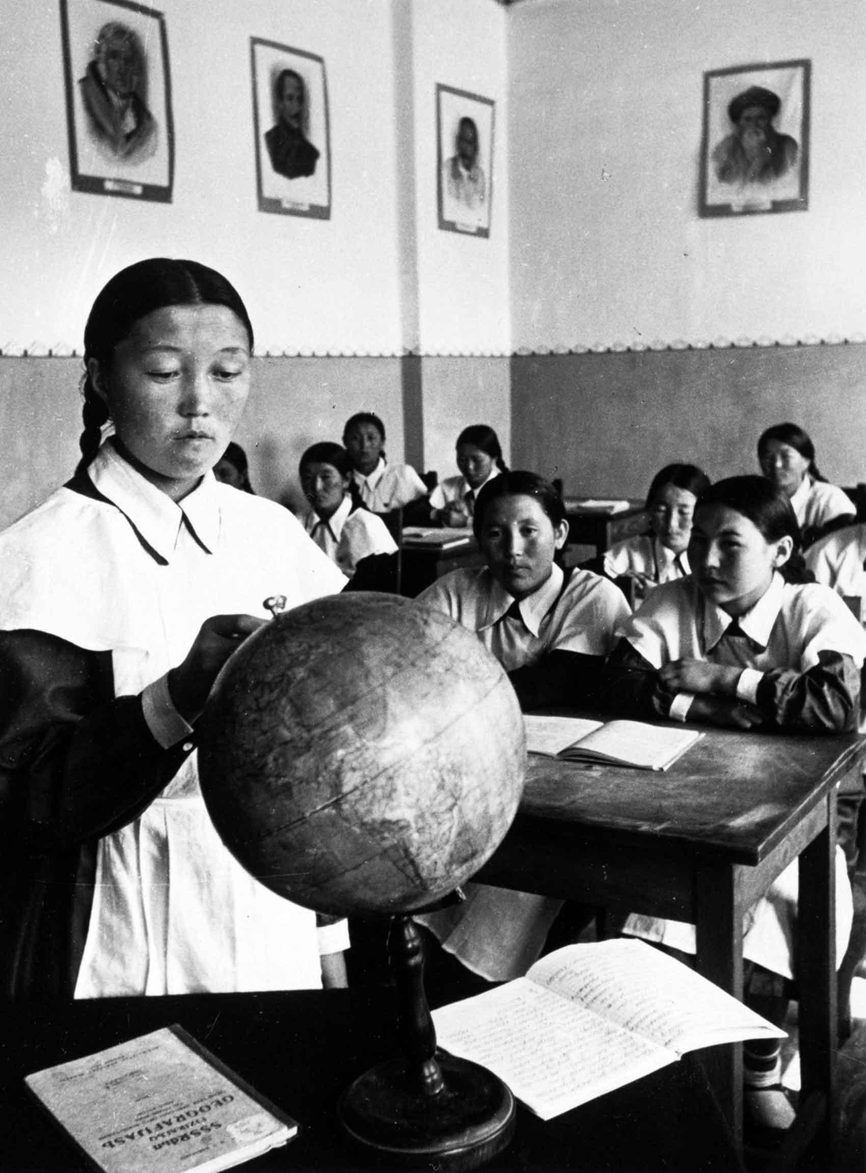 Woman standing at front of classroom and looking at globe