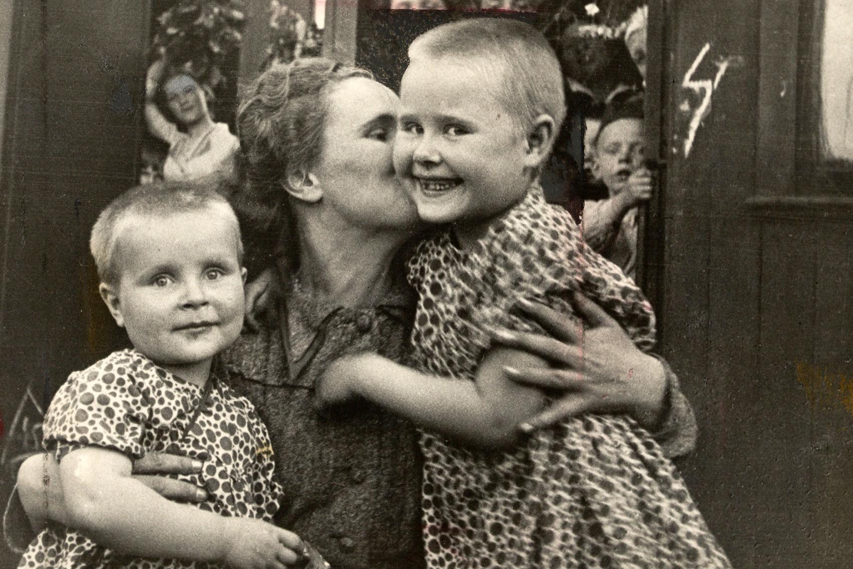 A woman embraces her children in front of train.