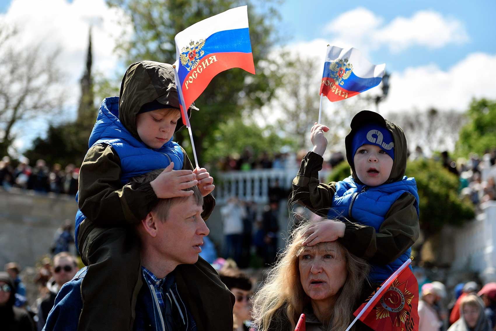 Two children, riding on adults' shoulders, wave Russian flags