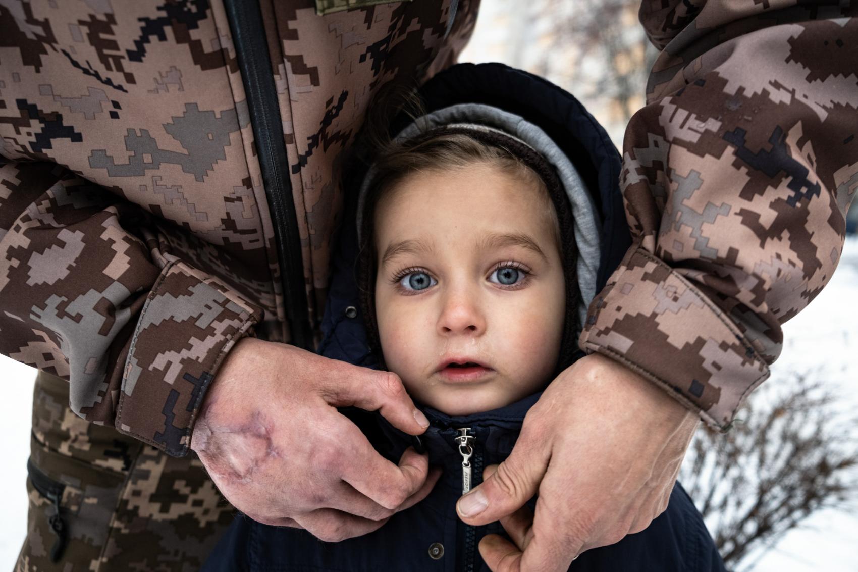 Sasha, a soldier of the Armed Forces of Ukraine, adjusting his three-year-old son Myron's zipper with a hand scarred by shrapnel during the Russo-Ukrainian war, Kharkiv, December 2022.