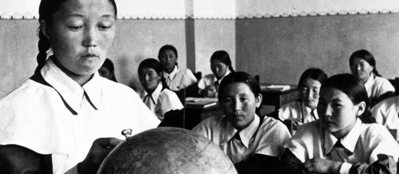 Woman standing at front of classroom and looking at globe