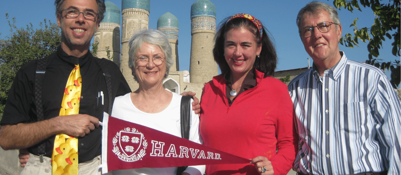 Ambassador Simons with three others in front of an Uzbek historical site holding a Harvard flag