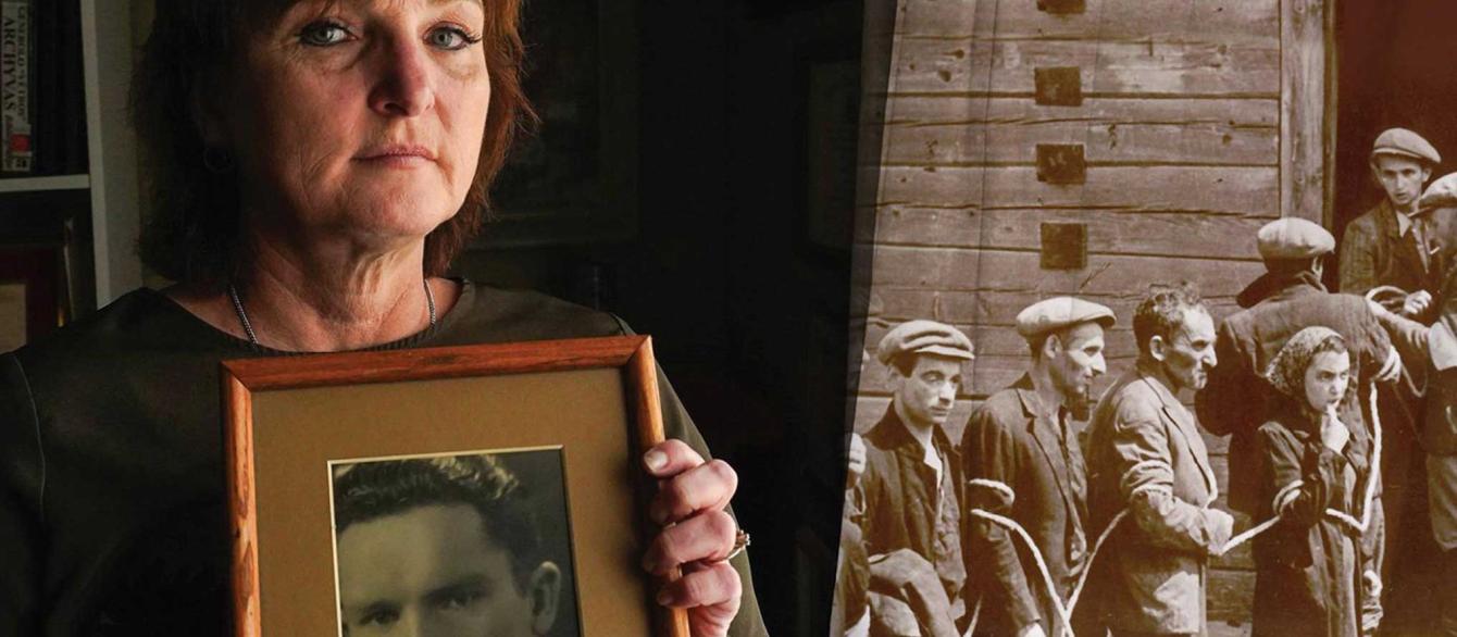 Silvia Foti holding framed picture of her grandfather with photo of Jewish prisoners in background