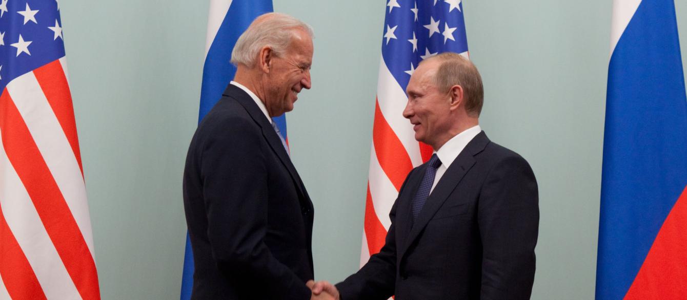 Joe Biden and Vladimir Putin shake hands with US and Russian flags in background