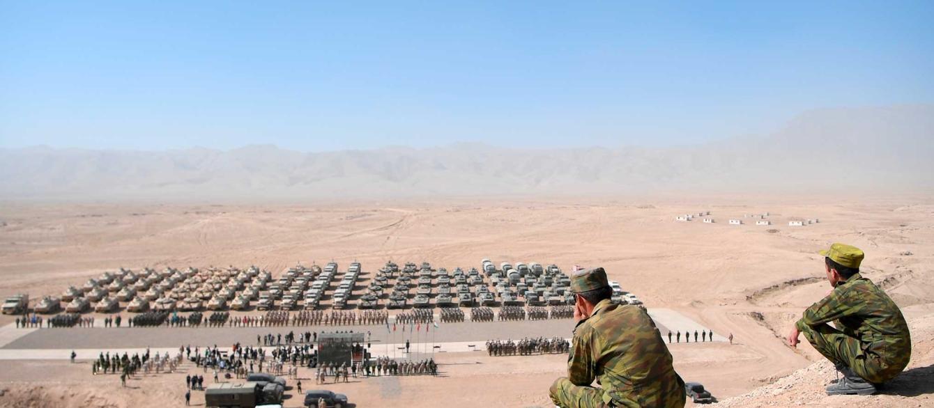 Crouching soldiers overlooking military drills in background