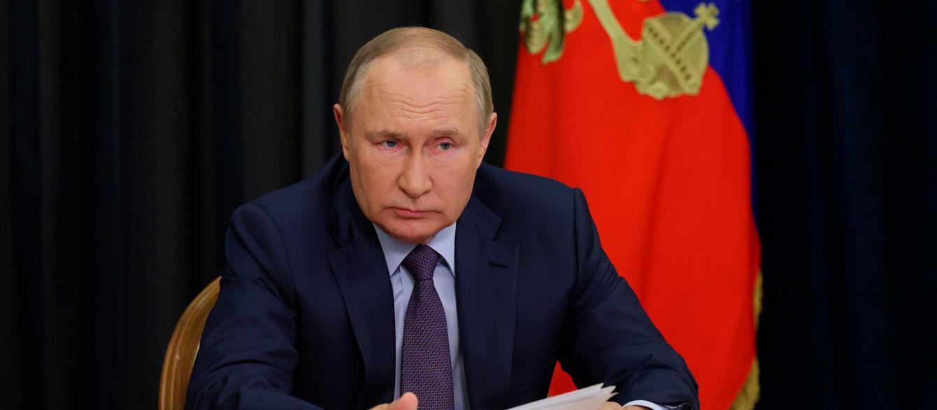 Russian President Vladimir Putin seated at table, gesturing