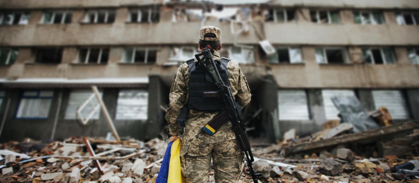 Ukrainian military woman with the Ukrainian flag in her hands on the background of an exploded house.
