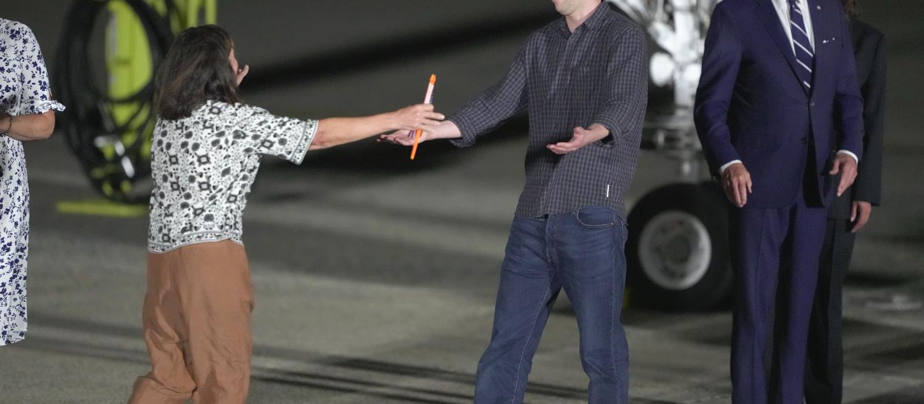 Reporter Evan Gershkovich is greeted on the tarmac by his mother, Ella Milman, as President Joe Biden and Kamala Harris look on at Andrews Air Force Base, Md., following his release as part of a 24-person prisoner swap between Russia and the United States, Thursday, Aug. 1, 2024. 