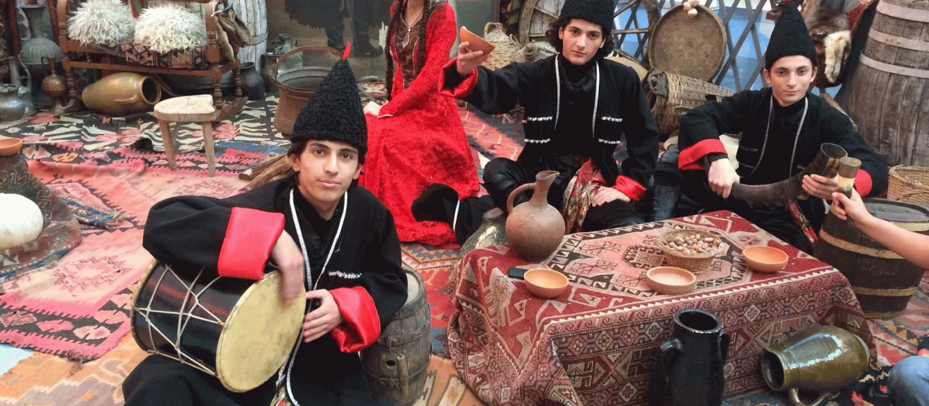 youth in traditional Georgian clothing sitting on the floor with music instruments