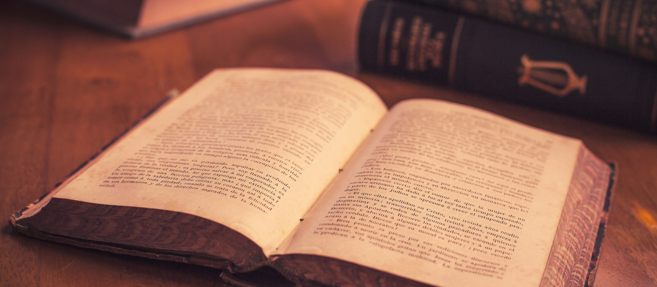 An open book set on a table with other books in the background.