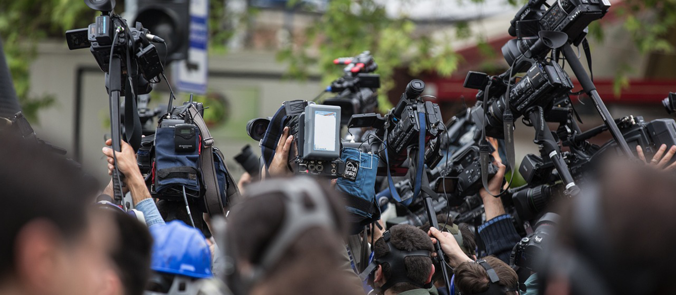 A crowd of journalists and camera-people crowd a street, ready to report.