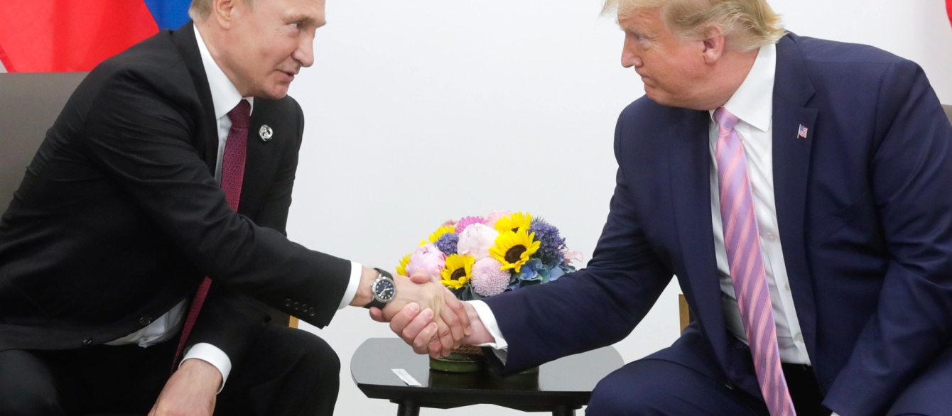 Vladimir Putin with President of the United States Donald Trump in front of flowers and each country's flag.