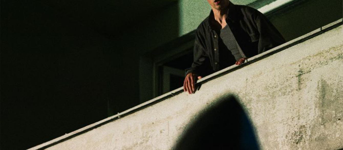 a man in the balcony, green background, and the shadowy figure in front