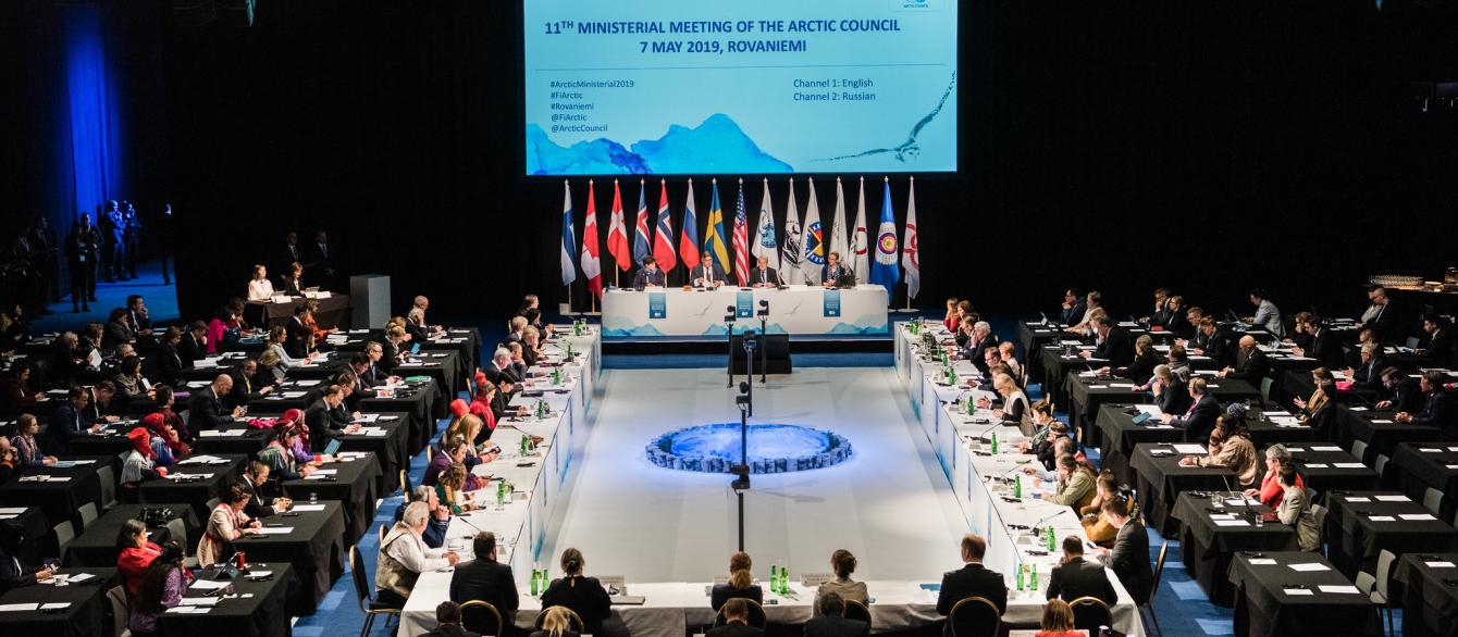 large room hosting Arctic Council meeting with screen for slides