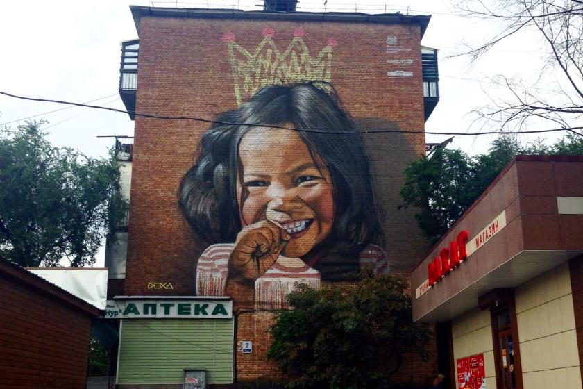 A mural on a brick wall of a smiling girl with a crown in Bishkek