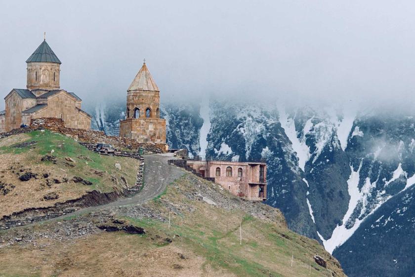 Medieval church on grassy hilltop surrounded by majestic mountains