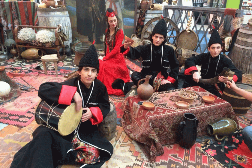 youth in traditional Georgian clothing sitting on the floor with music instruments