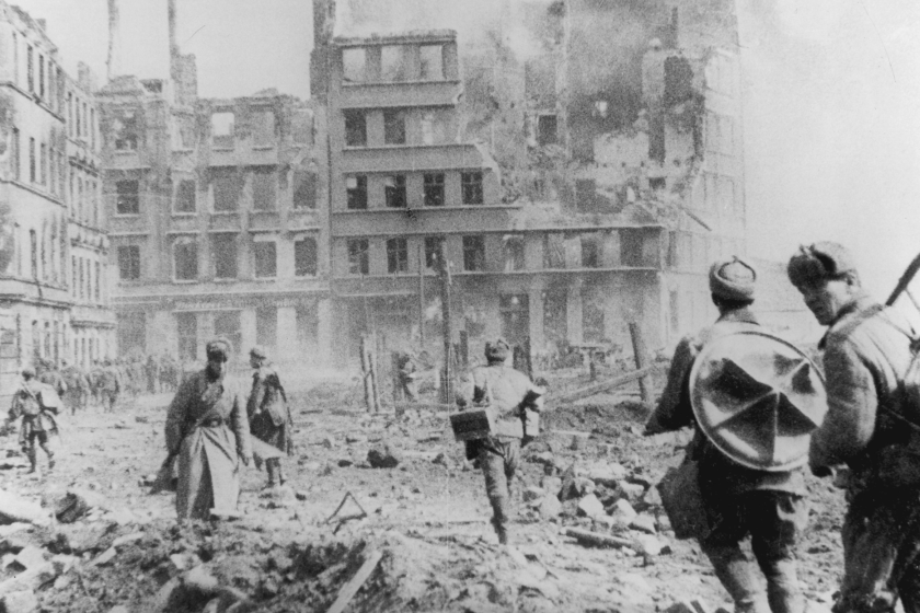 An image of WWII-era Germany, where a building crumbles ahead of a group of soldiers.