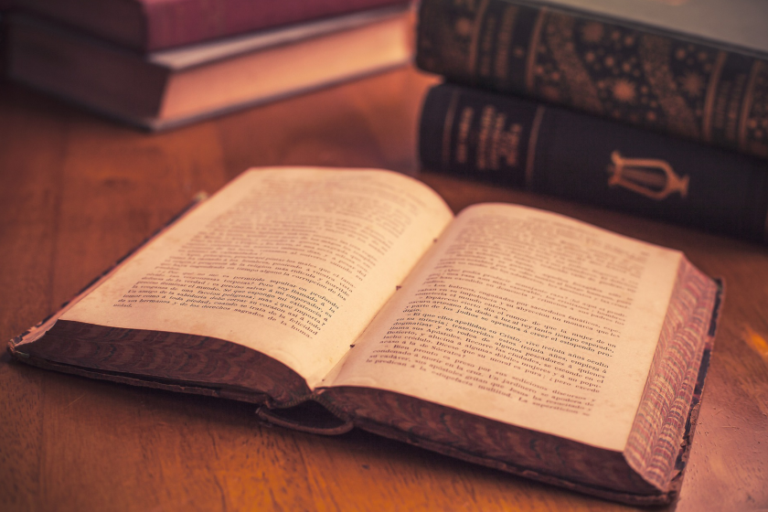 An open book set on a table with other books in the background.