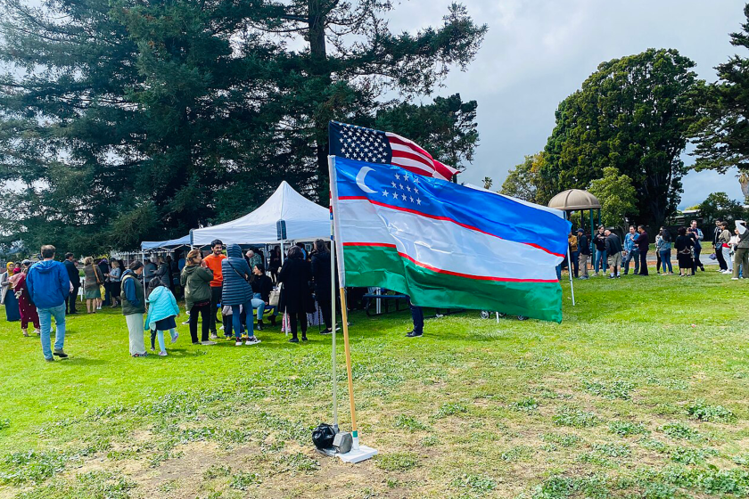 People gather at a festival with Uzbek and American flags at the center.