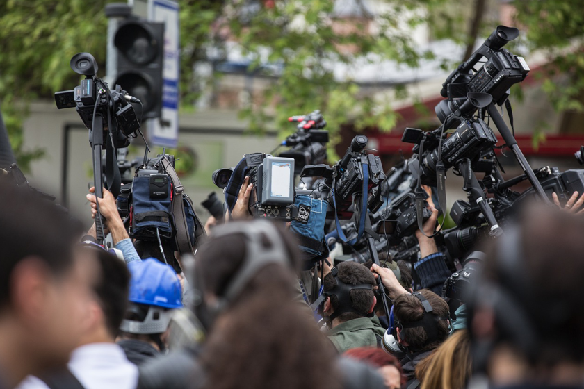 A crowd of journalists and camera-people crowd a street, ready to report.