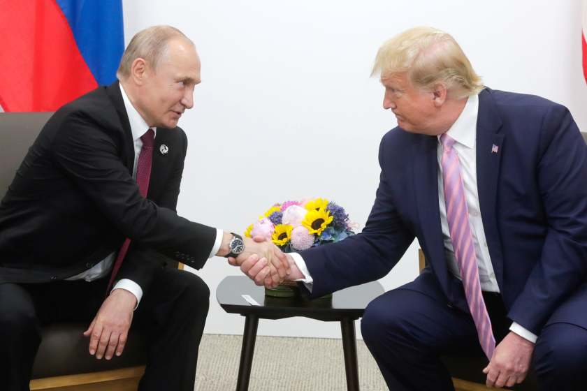 Vladimir Putin with President of the United States Donald Trump in front of flowers and each country's flag.