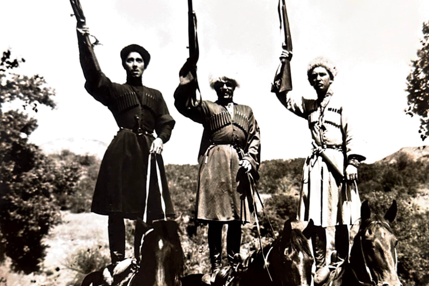 Three people standing on horses with guns to the air