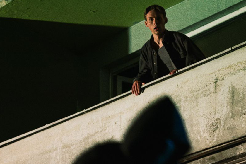 a man in the balcony, green background, and the shadowy figure in front